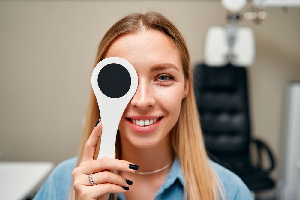 An optometrist helps a patient try on glasses while sitting at a desk with a computer displaying eyewear options - Carlson Eye Care - Eye Doctor Grandville MI